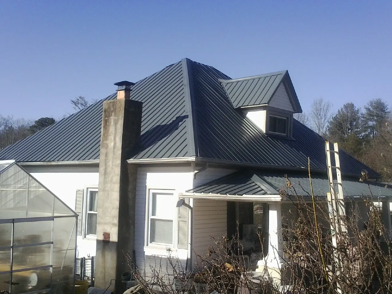 Dark blue standing seam metal roof on a white farmhouse with dormer — Slate & Tile Roof Repair by Roofing Brothers in Hill