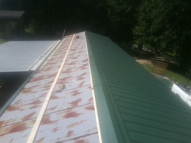 Old rusted panels beside newly installed green metal roofing — Wind Damage Roof Repair by Roofing Brothers in Hill