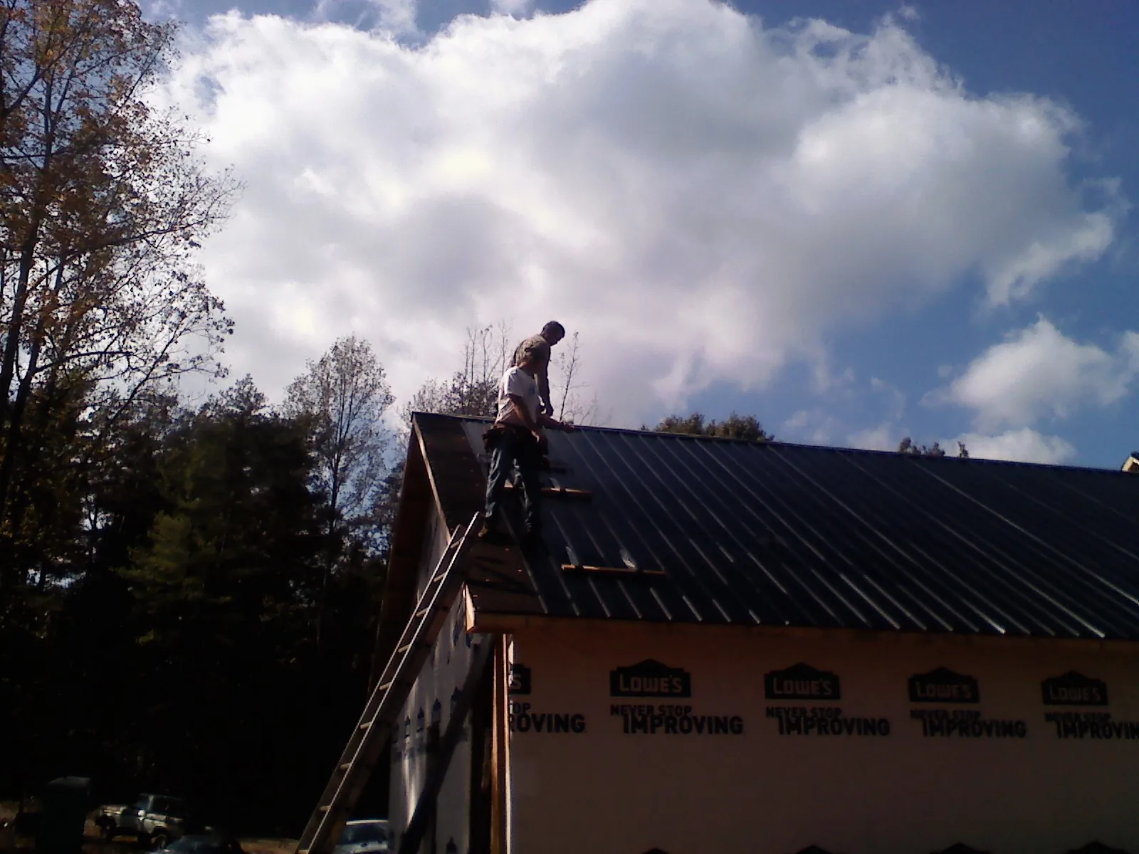 Roofer fastening dark metal panels high against a cloudy sky, from a Roof Inspection job in Hill