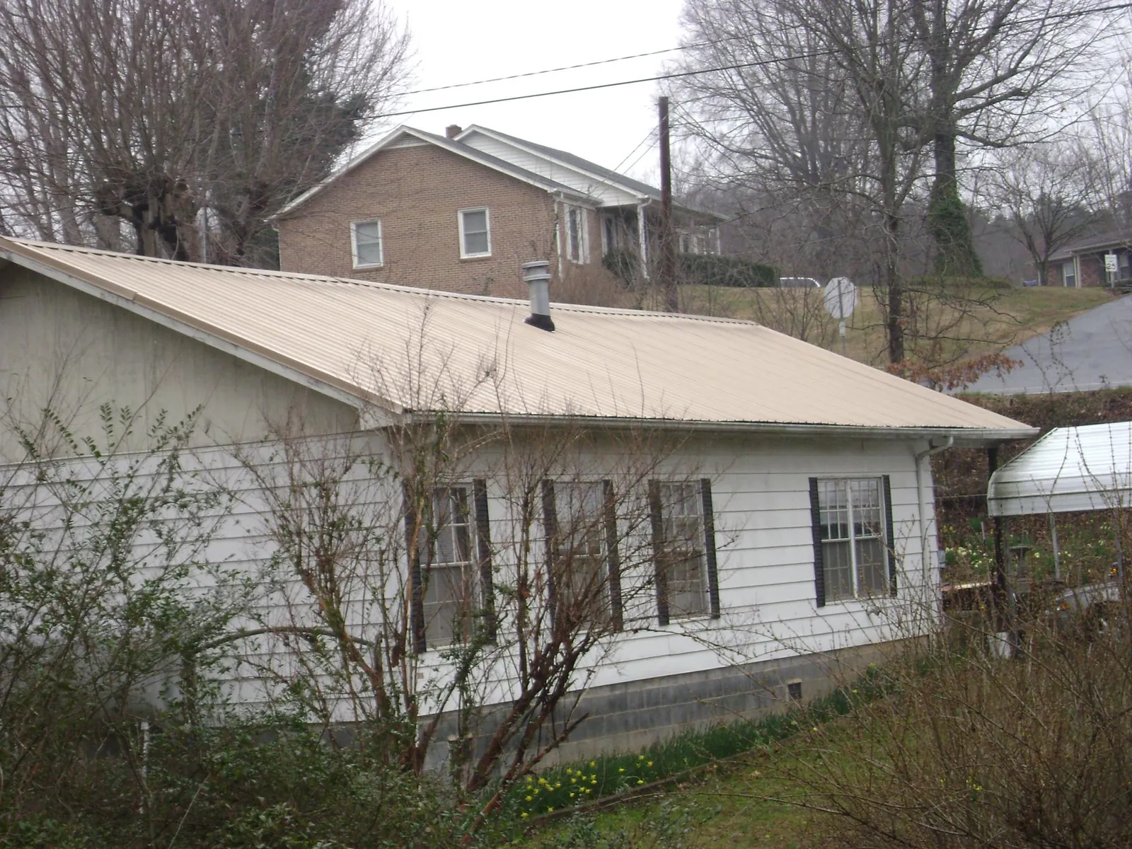 Tan metal roof on a white sided house set into a hillside — Commercial Roofing by Roofing Brothers in Hill