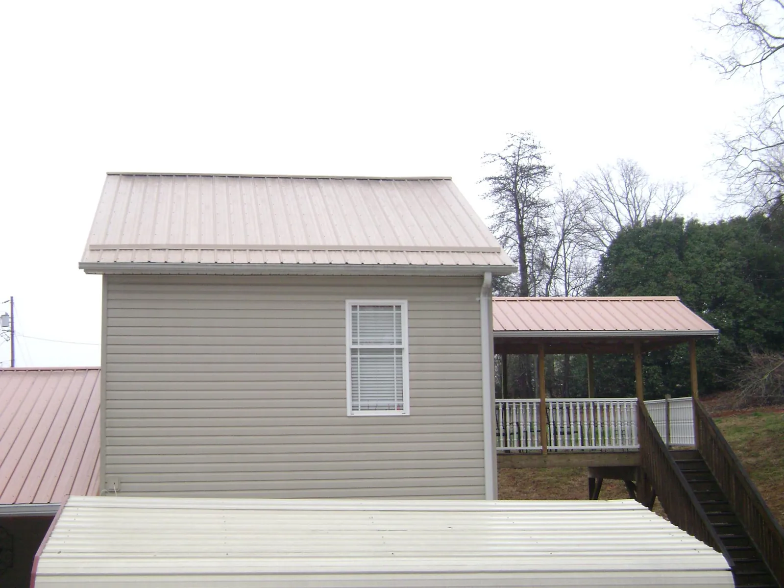 Tan metal roofs on a two story addition and attached porch, from a Roof Replacement job in Hill